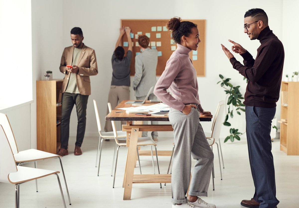Five professionals collaborating around a wooden table and sticky-note corkboard in a bright modern office