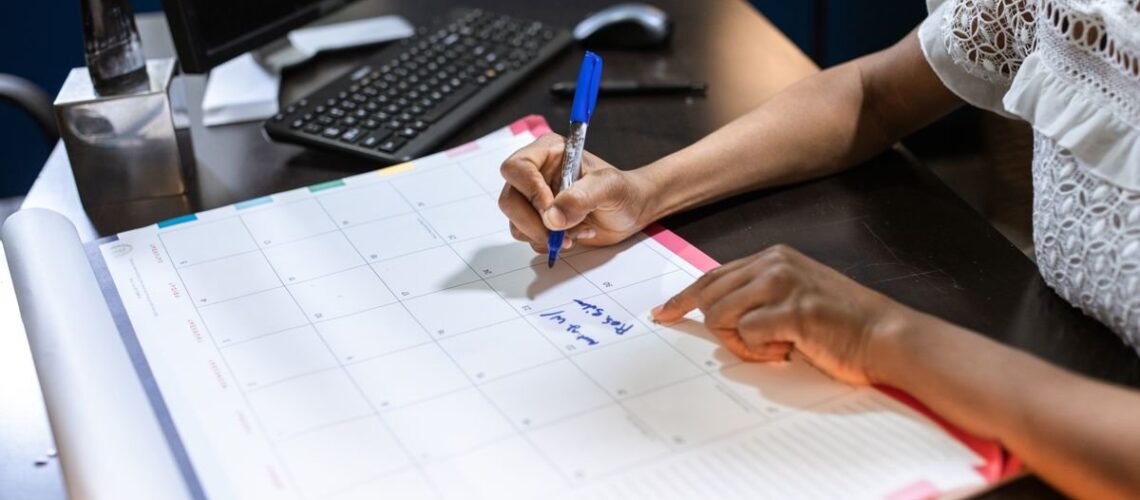 A person writing notes on a desk calendar with a pen