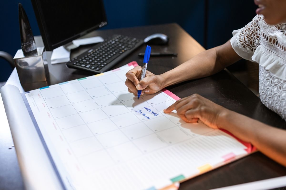 A person writing notes on a desk calendar with a pen